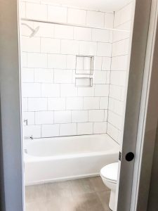 Photo from a custom home tour. This photo shows a picture of a bathtub with large white tile laid in a subway pattern with dark gray grout.