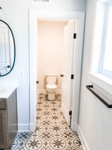 Custom home tour photos. This photo shows a toilet in a separate water closet. The toilet is white and the flooring has a gray and white patterned tile.