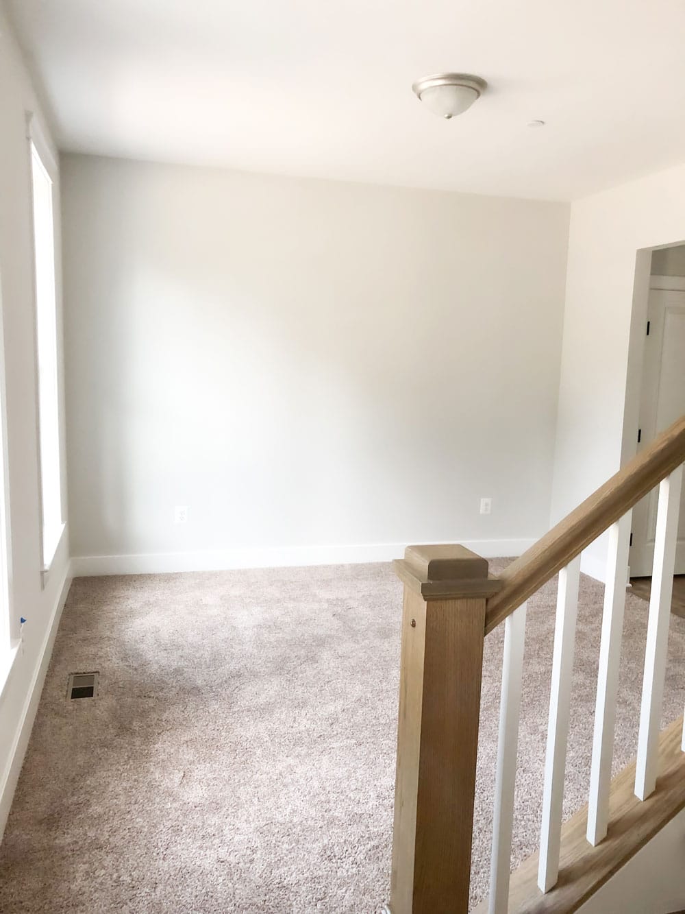 Custom home tour photos. This photo shows the playroom in the home. It has a neutral beige looking carpet, white walls, and a single ceiling light. 