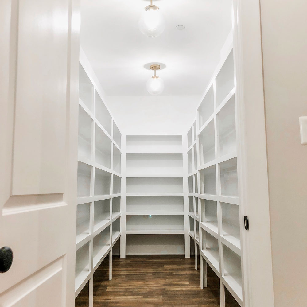 Custom home tour photos. This photo shows the large walk-in pantry.. It has white shelving from floor to ceiling and luxury vinyl flooring that looks like wood. 