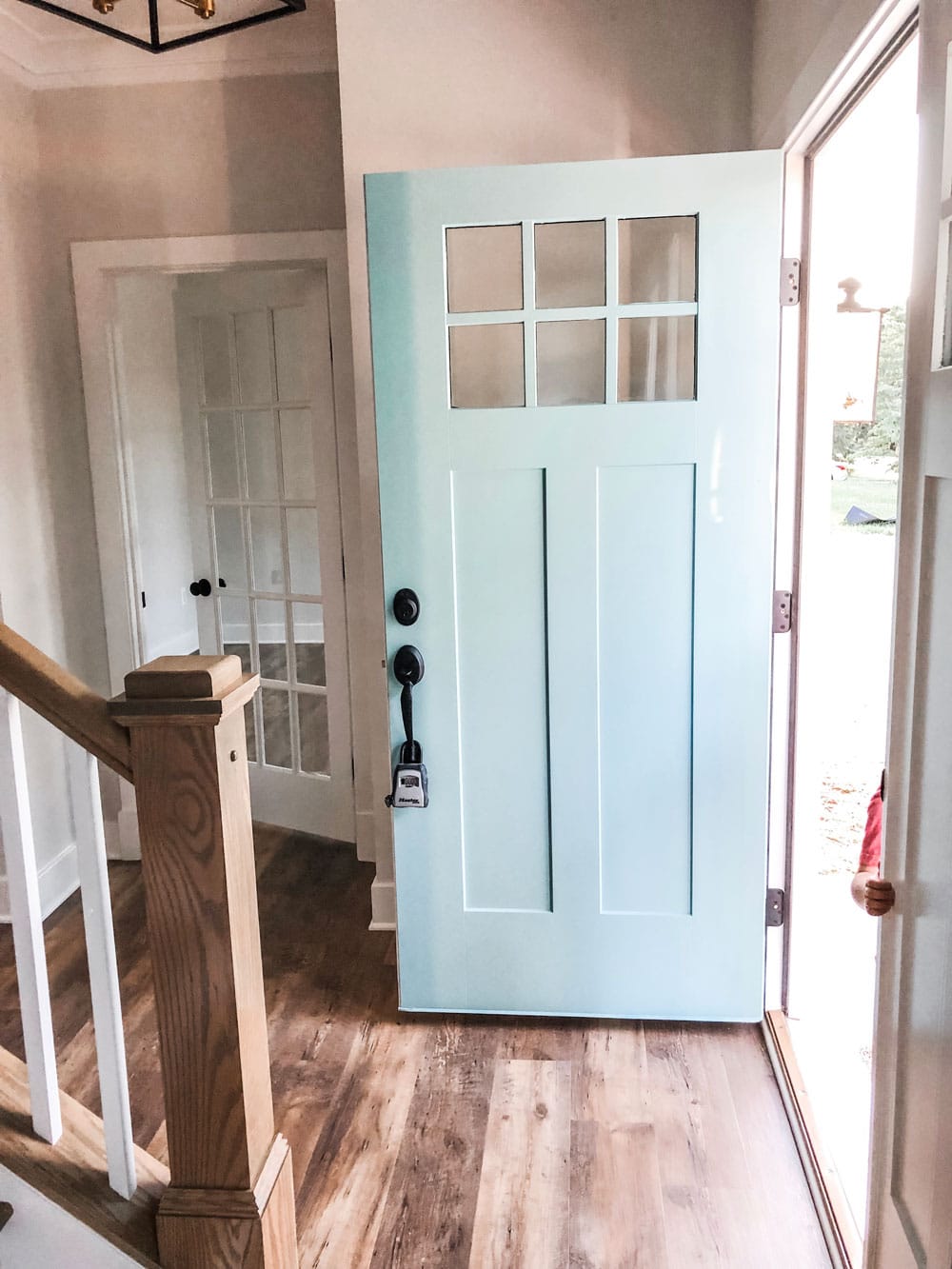 Custom home tour photos. This photo shows the front door opened into the foyer. The front door is a blue color and has a black handle. It has a small 6 pane window at the top of the door. 