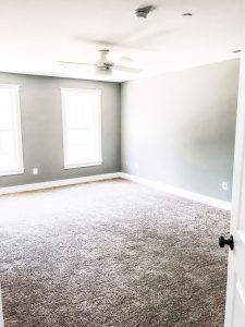Custom home tour photos. This photo shows the master bedrooms. It has gray walls and beige carpet. There is a white ceiling fan as well and two large windows.