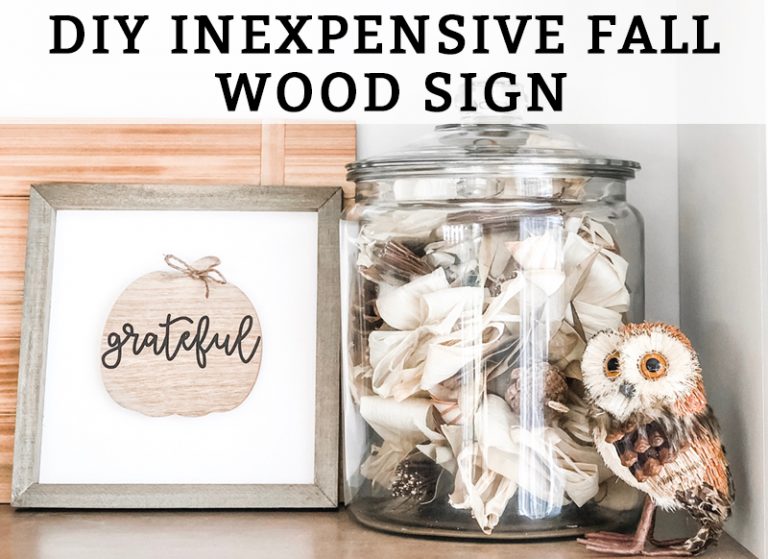 This DIY inexpensive fall wood sign is picture. It's an image of a wood sign with a light wood frame, white background, wood pumpkin, and the words grateful written in black cursive across the pumpkin. A small twine bow is on the stem of the pumpkin. The words, DIY Inexpensive Fall Wood Sign are on the top of the sign.