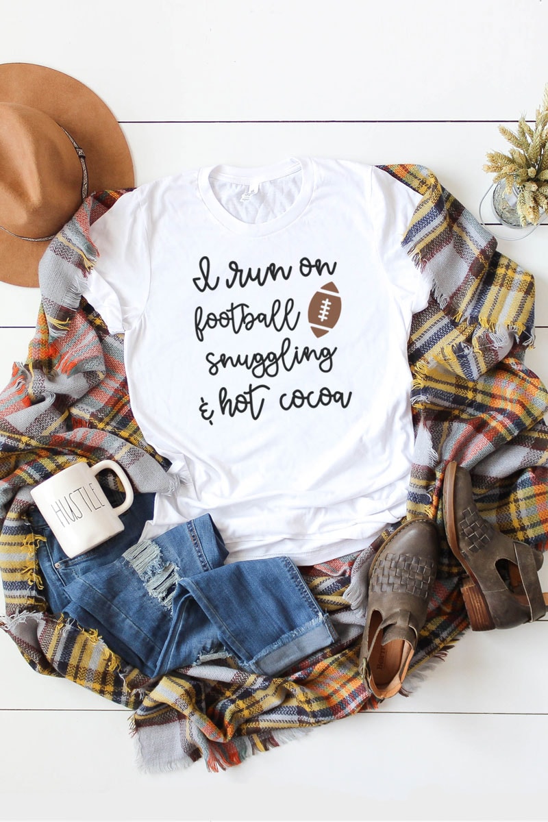 This picture represents an example of the free fall svgs included in this set. This is just one of the options available involving the phrase I Run On... White t-shirt laying on a brown, yellow, orange, and white, plaid blanket. There is a white mug that says hustle in the bottom left on top of a pair of ripped up blue jeans. There are also a pair of brown booties on the far right bottom corner and a tan hat in the top left.