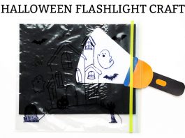 Halloween Flashlight Craft for Kids Image of a ziploc bag with a haunted house, ghosts and bats drawn on it. It has a black background in the bag and a flashlight paper placed inside of the bag just in front of the black paper, highlighting one of the ghosts.