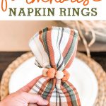 At the top of the image, it says: DIY fall farmhouse napkin rings. Underneath, there is an image of the napkin ring. The image is of DIY Thanksgiving napkin rings. They're plaid green, orange, and white napkins with mini pumpkins and wood beads around the napkins.