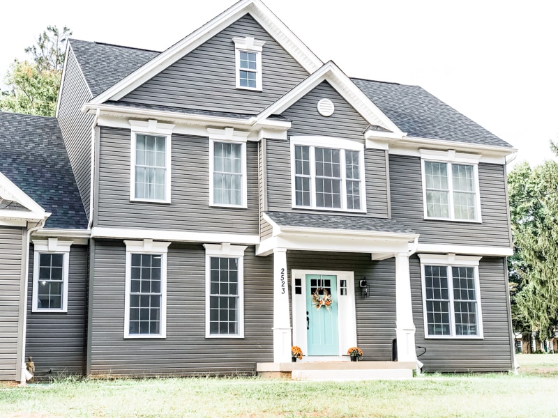 Picture of a dark gray house with a blue door. There is a small front porch with two white columns.