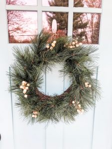 #shop This image shows a green wreath on a blue door. The wreath has small white berry looking clusters on it.