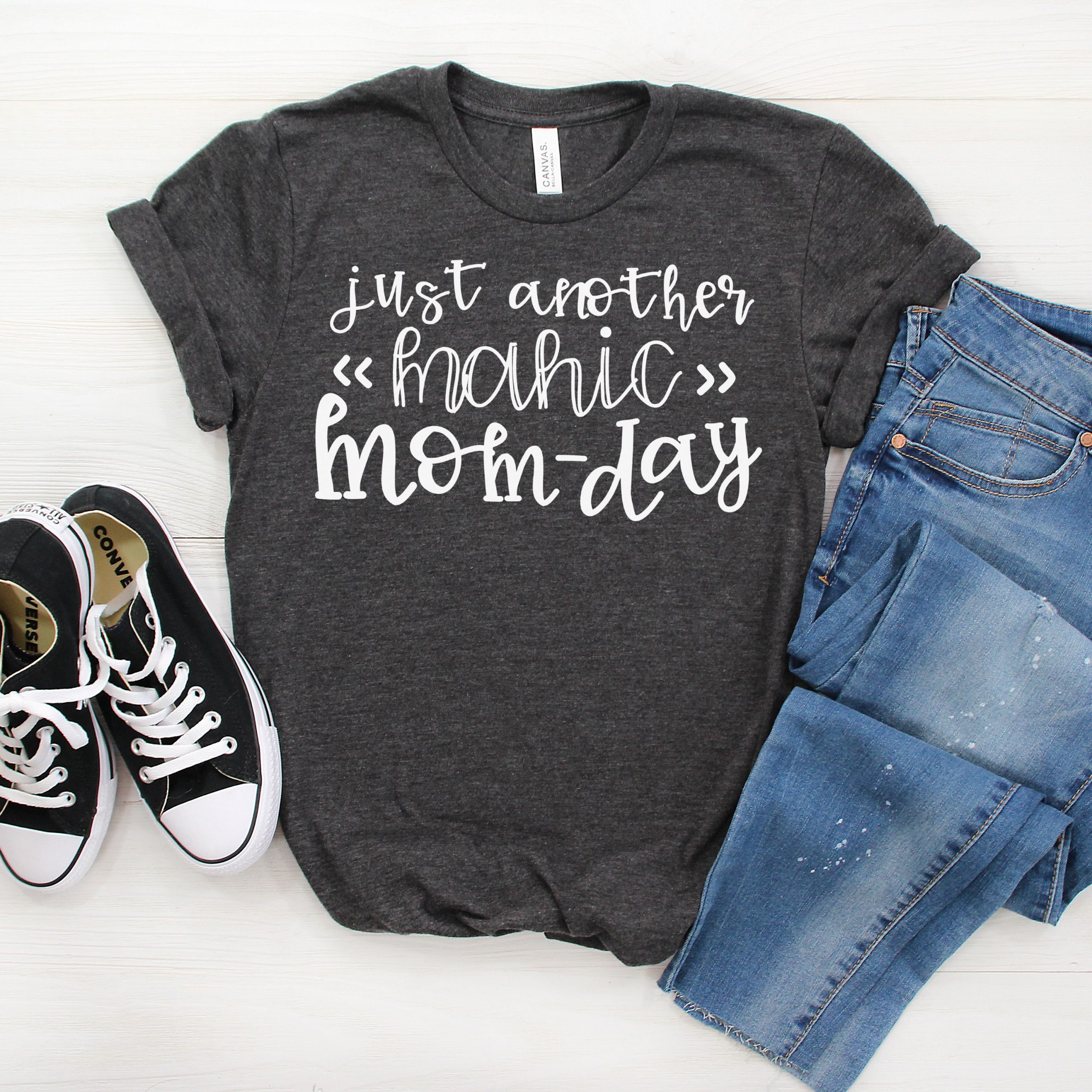 Free Manic Mom Day SVG example. The picture is of a gray t-shirt with the words, Just another Manic Mom-Day. Next to a pair of blue jeans and black converse sneakers.