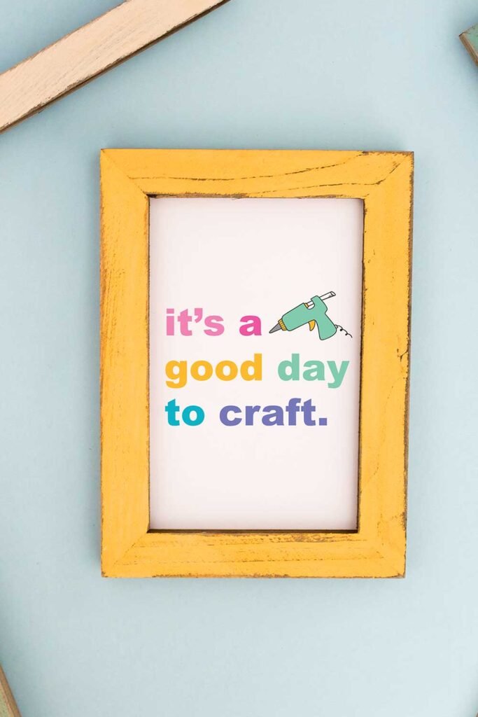 Blue background with a yellow picture frame. The inside of the picture frame says it's a good day to craft with the picture of a hot glue gun.