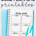Pinterest graphic titled “Free 2026 Goal Planning Printables,” showing a spiral notebook open to a 2026 goals worksheet with pens resting on the page and a bright blue notebook underneath.