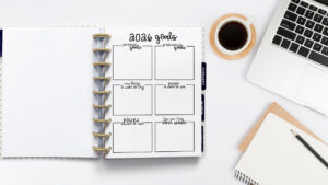 2026 goals worksheet in a discbound planner on a clean workspace with a laptop, notebook, pencil, and cup of coffee, featuring boxes for personal goals, professional goals, new things to try, people to see, places to visit, and helping others.