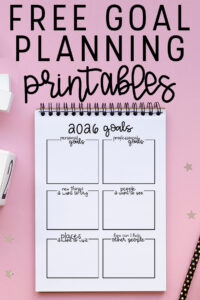 Graphic with the text &ldquo;Free Goal Planning Printables&rdquo; above a spiral notebook displaying a 2026 goals worksheet on a pink background with decorative stars.