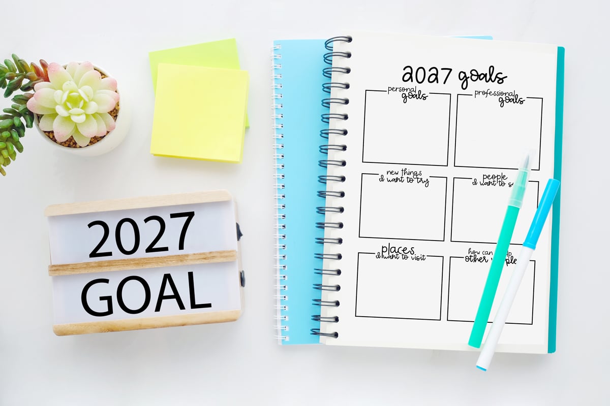 Goal-Setting-Worksheets-2027-Example-sign 2027 goals worksheet in a spiral notebook on a white desk with teal and white pens, a succulent plant, sticky notes, and a