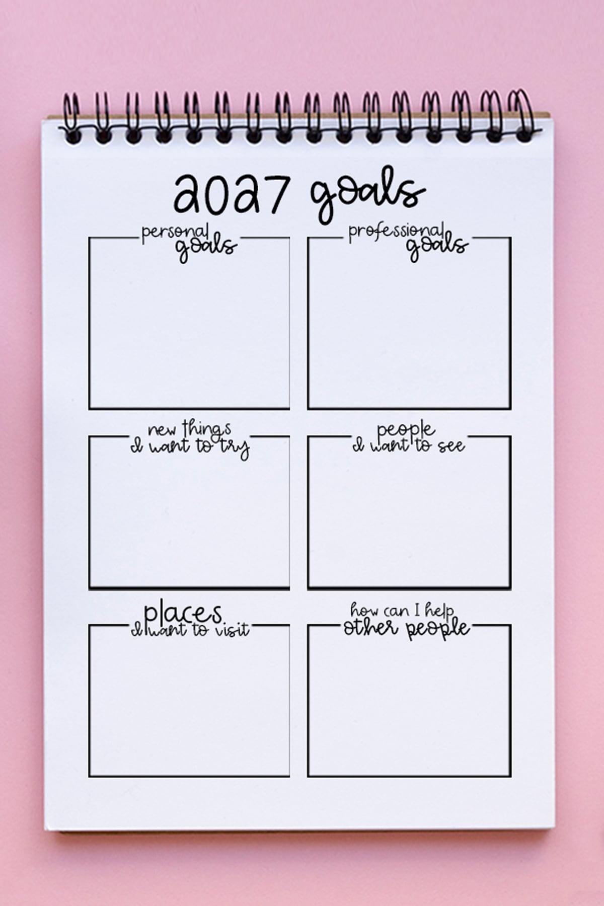 Goal-Setting-Worksheets-2027-Example 2027 goals worksheet in a spiral notebook on a pink background, showing blank boxes for personal goals, professional goals, new things to try, people to see, places to visit, and ways to help others.