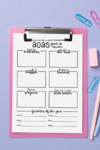 2025 year-in-review worksheet on a pink clipboard against a lavender background, surrounded by pastel pens, erasers, and paper clips. The page includes boxes for memories, lessons, bumps in the road, projects, and yearly favorites.