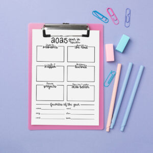 2025 year-in-review worksheet on a pink clipboard over a lavender background, styled with pastel pens, sticky erasers, and paper clips arranged around the page.