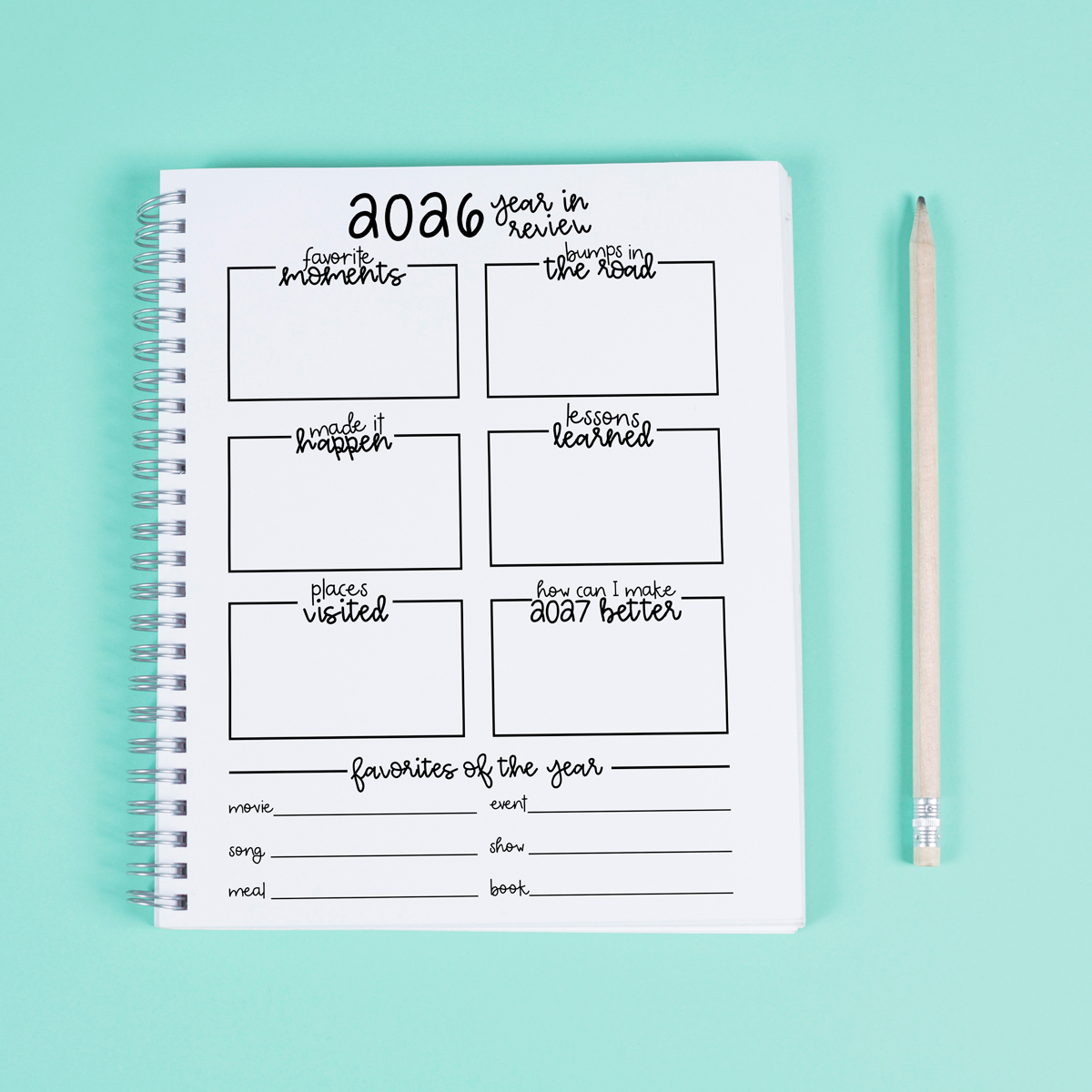 2026 year-in-review worksheet in a spiral notebook on a mint green background with a wooden pencil beside it, featuring sections for favorite moments, lessons learned, places visited, and favorites of the year.