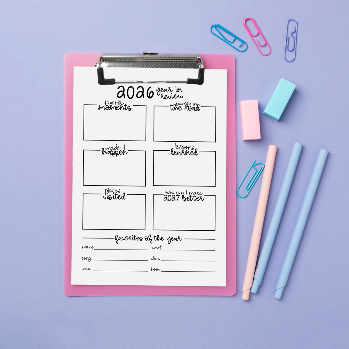 2026 year-in-review worksheet on a pink clipboard against a lavender background, styled with pastel pens, erasers, and colorful paper clips. The page includes boxes for memories, lessons, challenges, projects, and yearly favorites.