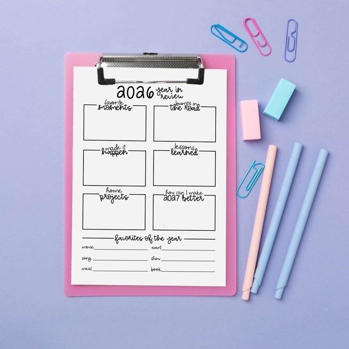 2026 year-in-review worksheet on a pink clipboard over a lavender background, styled with pastel pens, sticky erasers, and paper clips arranged around the page.