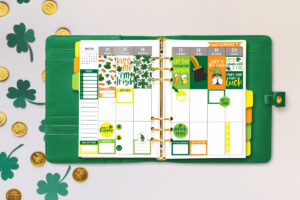 This image shows some of the available free Saint Patrick's Day stickers you can download at the end of this post.It shows a sample of an open green planner with some of the free stickers you can download. The planner is resting on some paper four leaf clovers and gold coins.