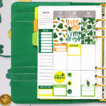 This image shows some of the available free Saint Patrick's Day stickers you can download at the end of this post.It shows a sample of an open green planner with some of the free stickers you can download. The planner is resting on some paper four leaf clovers and gold coins.