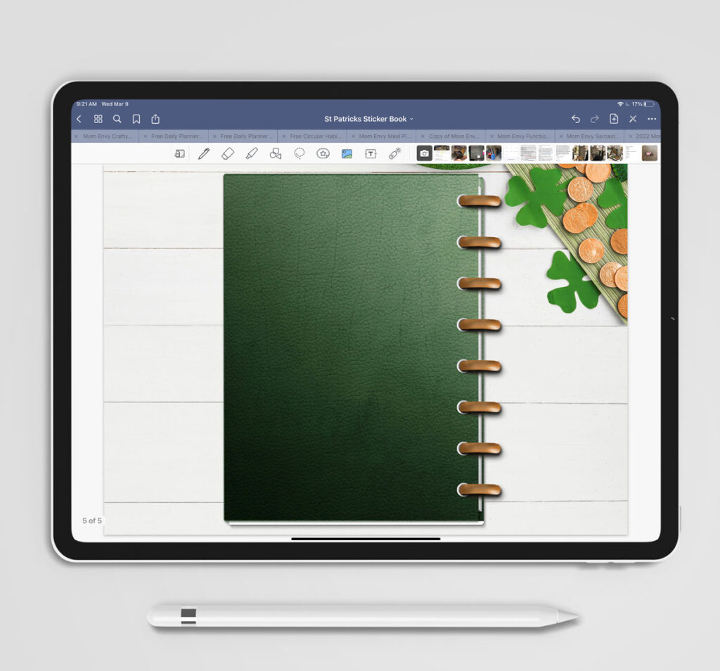 This image shows some of the available free Saint Patrick's Day stickers you can download at the end of this post. It shows an iPad and Apple Pencil. The screen is shows a Goodnotes program with a closed green planner. The planner is resting on some paper four leaf clovers and gold coins.