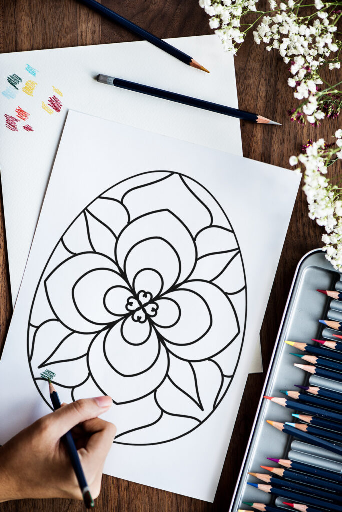 This image shows one of the Easter Egg coloring pages designs you can download for free at the end of this blog post. It shows a person coloring a mandala Easter egg coloring page.