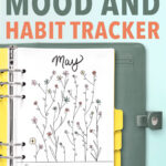 The top of this image says Free Floral Mood and Habit Tracker. Below that is a blue-green planner with silver rings opened up to the free May Mood tracker you can download at the end of this blog post. The tracker is filled in with various colors. There is a Key at the bottom of the tracker that says - blue for sad, reddish orange for anxious, yellow for happy and pink for content.