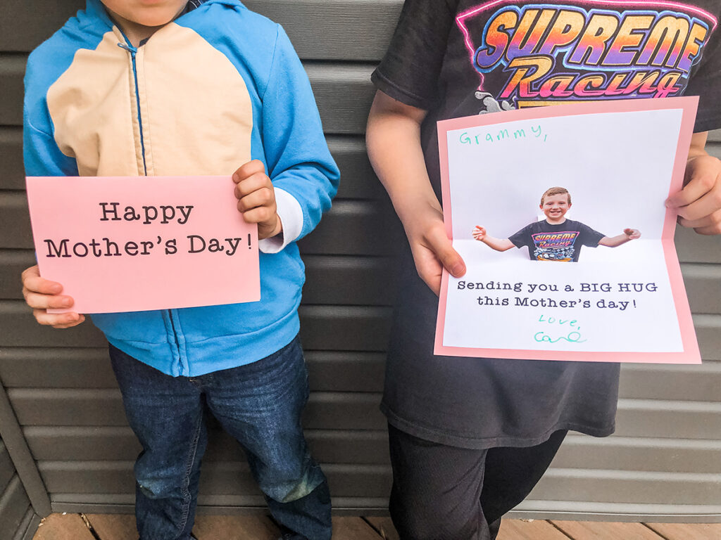 This image shows two children holding the pop up mother's day cards diy. One child is holding the card closed, it reads “Happy Mother’s Day!” The other child is holding the card open, it reads “sending you a BIG HUG this Mother’s day!”