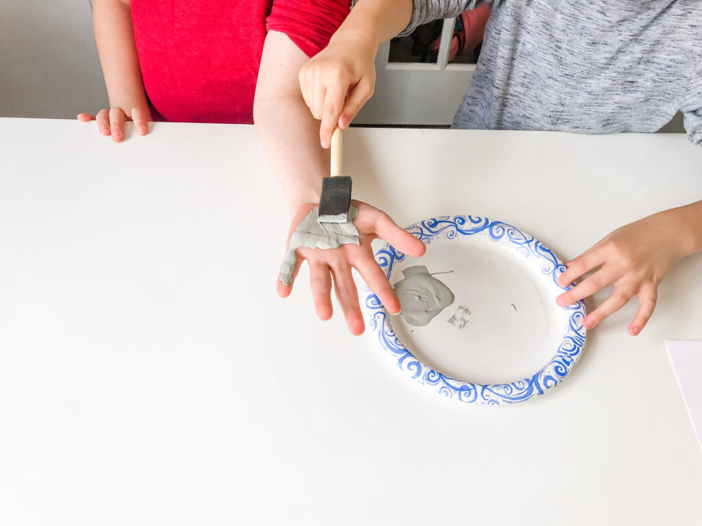 This image shows gray paint being painted onto the palm of a child's hand.