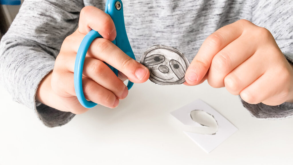 This image shows a child holding a colored in and cut sloth head.