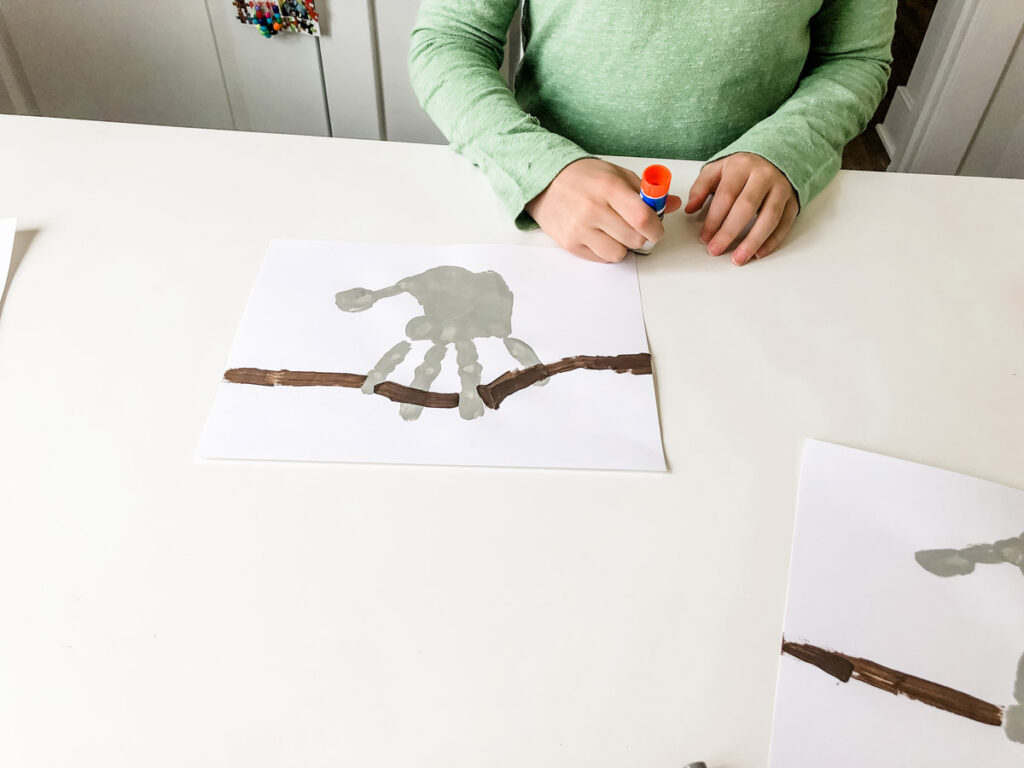 This image shows a child placing glue on the back of the sloth head.