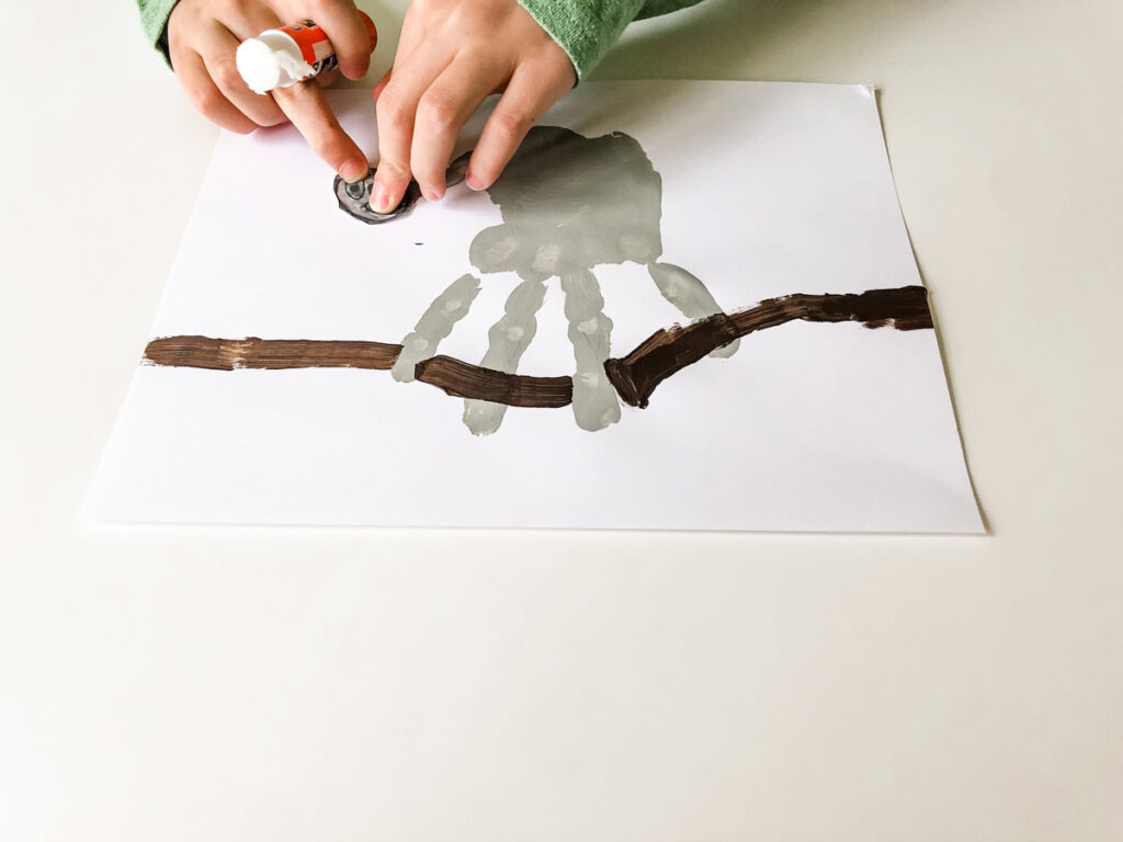 This image shows the child placing the sloth head on top of the thumb on the gray handprint.