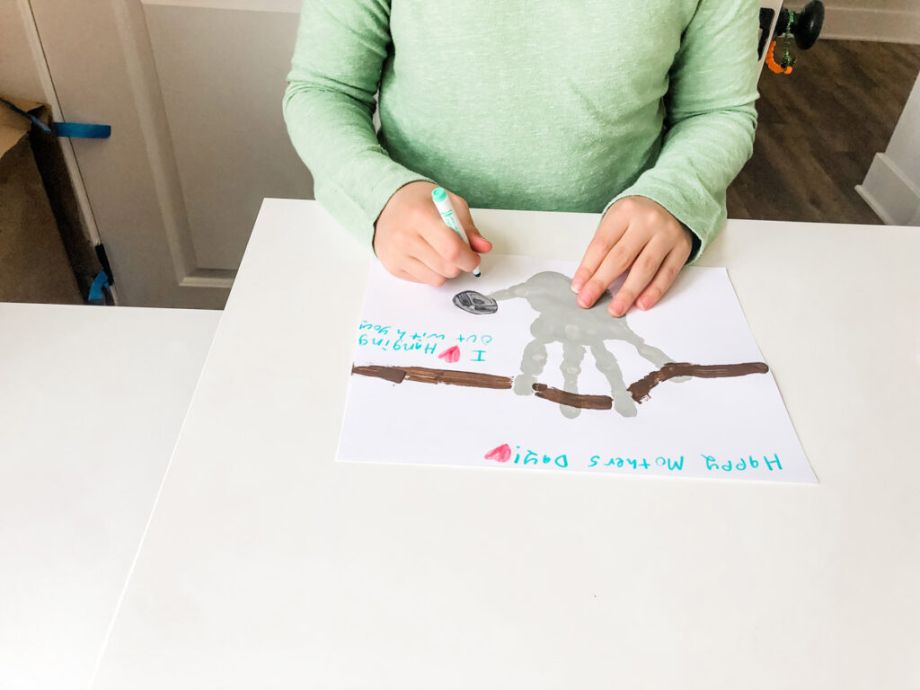 This image shows a child signing their name on the sloth handprint craft.