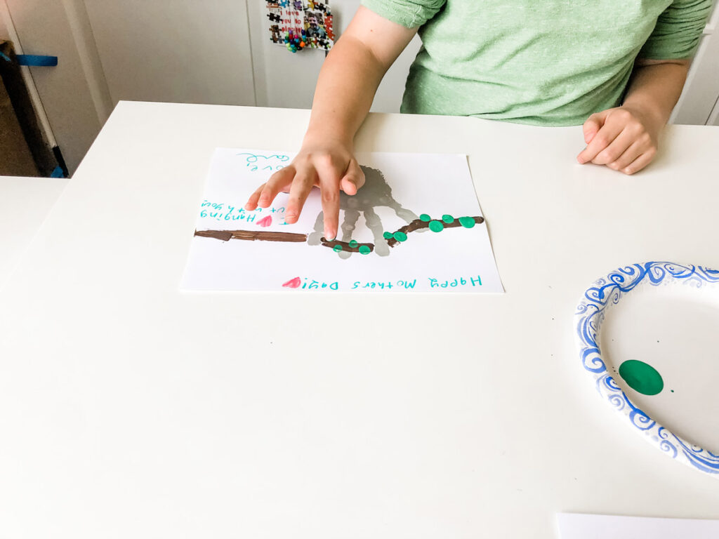 This image shows the child using green paint painted on their finger tips to press on to the branch to create green leaves out of their fingerprint.