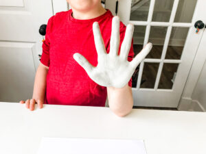 This is the image of a child holding up their hand painted in gray paint.