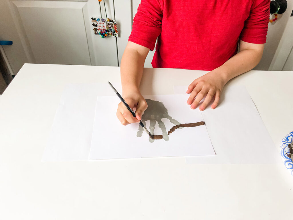 This image shows a child drawing a brown branch through the fingers of the gray handprint.