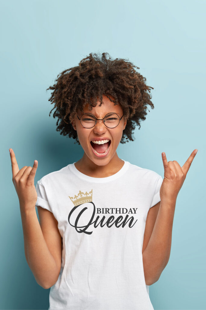 This image shows an example with one of the free svgs you can get in this blog post. It shows a girl wearing a white t-shirt with a Birthday Queen SVG. She is up against a blue background.