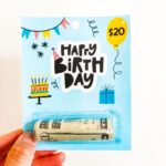 This image shows the free chapstick money holder template holding a $20 bill. The template says Happy Birthday with a balloon in the top right corner with $20. The template also includes a birthday cake with candles, a gift box, a banner, and a party hat on the B.