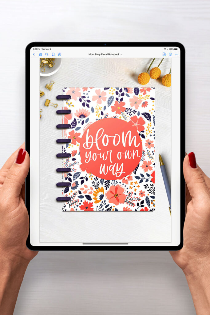 This is an image of a woman holding an iPad. The iPad is opened up to the first page of the free Digital Notebook you can download for free at the end of this post. The notebook has a floral design with the quote, “bloom your own way” on it.