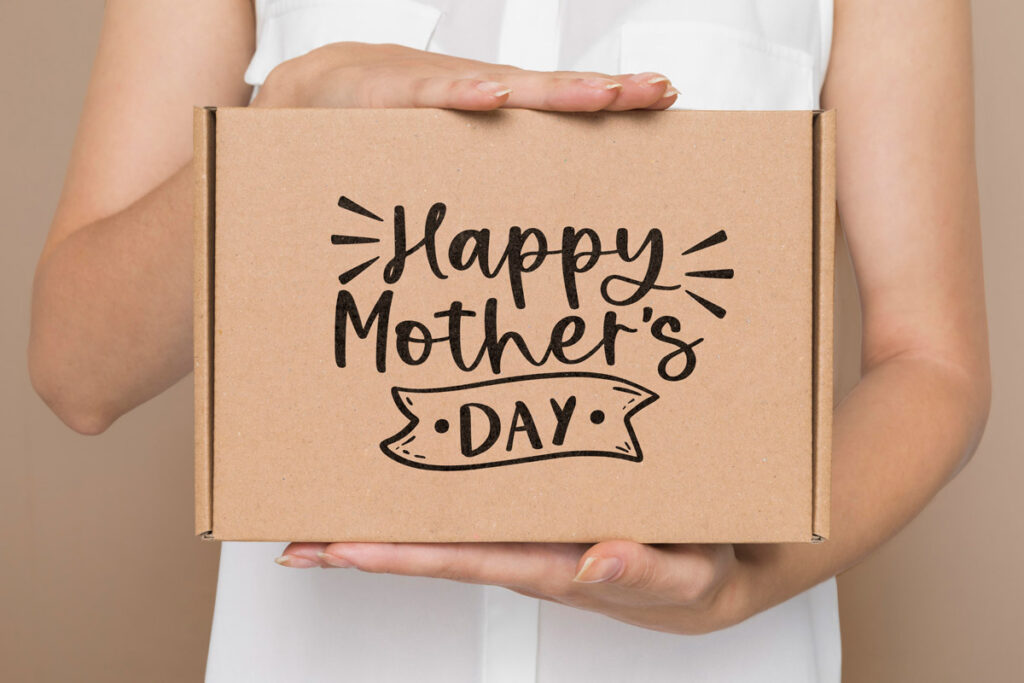 This is an image of the free Happy Mother's Day SVG you can download at the end of this post. It's a woman holding a brown kraft gift box with the words, Happy Mother's Day on it.