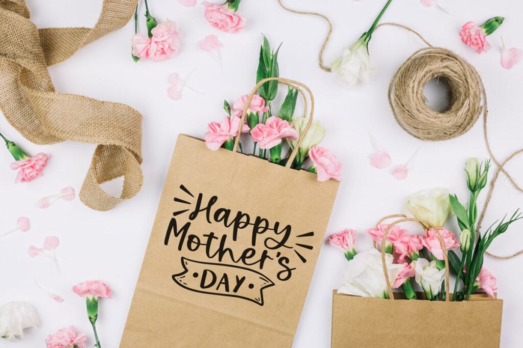 This is an image of the free Happy Mother's Day SVG available to download at the end of this post. The file is shown on a brown craft gift bag that is filled with pink carnations. The bag itself says Happy Mother's Day.