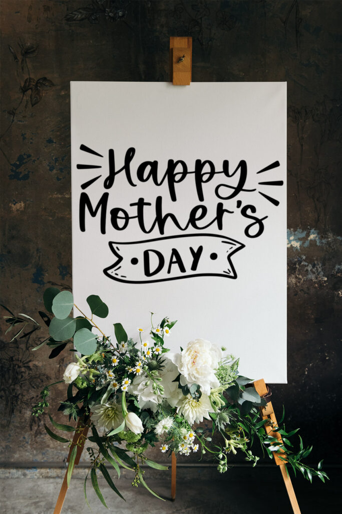 This is an example of the free Happy Mother's Day SVG on a white sign with some green and white florals attached to the sign. The sign itself reads, Happy Mother's Day.