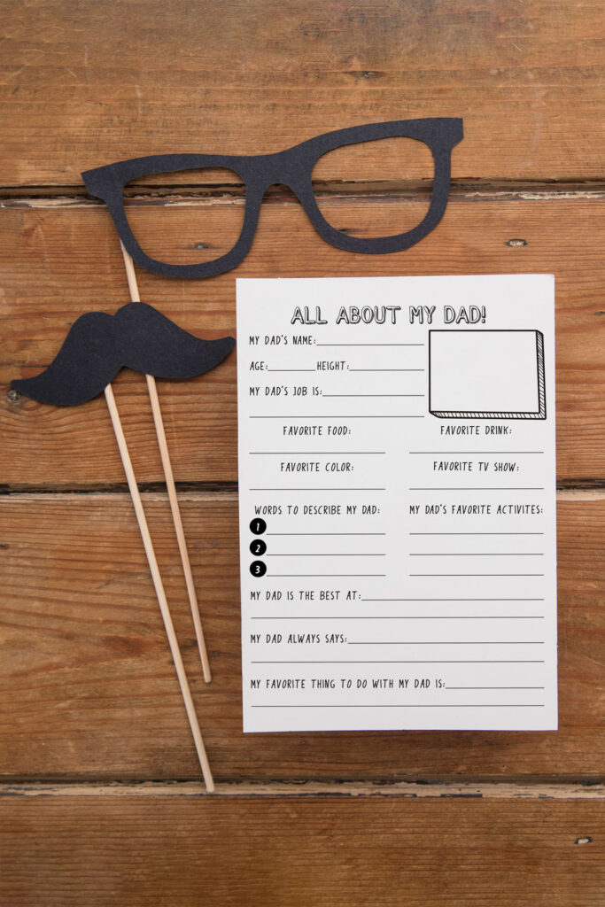 This image shows the free Father’s Day questionnaire you download for free at the end of this blog post. It is laying on a wood table top. Next to it are a paper mustache and paper glasses on a stick.