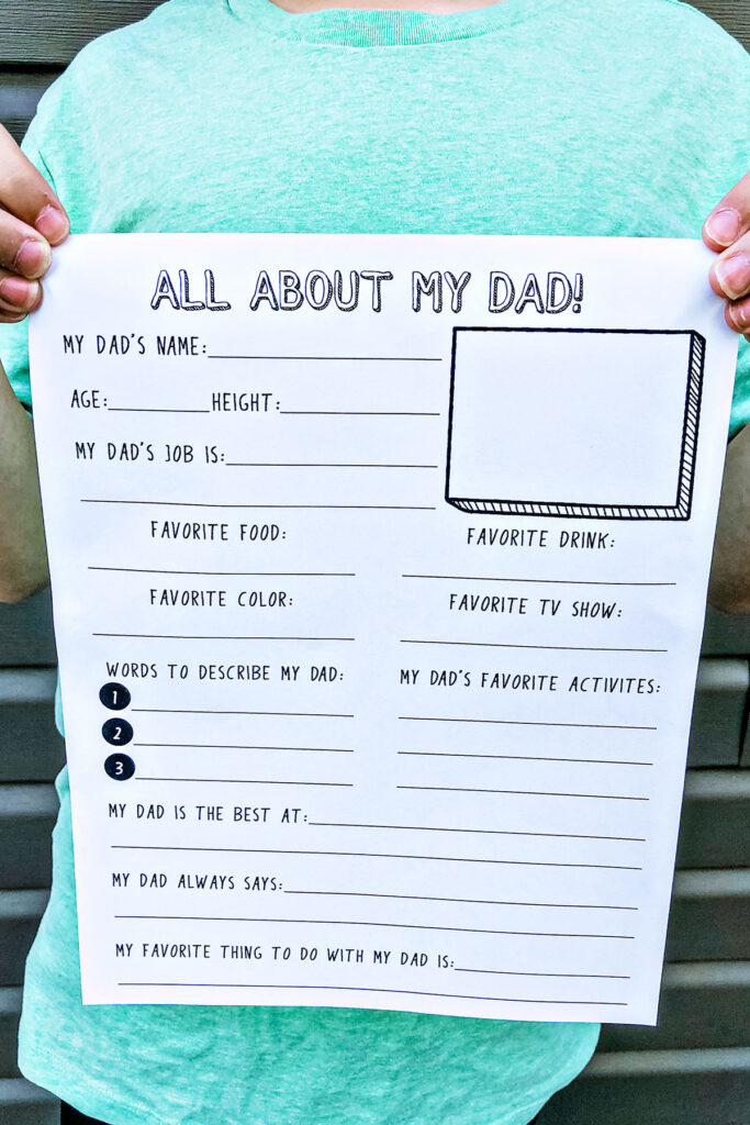This image shows the free Father’s Day questionnaire you download for free at the end of this blog post. A boy in a green shirt is holding the printable up. At the top the printable says: All About my Dad. Then has the following questions: My Dad’s name, Age, height, My Dad’s Job, favorite food, favorite drink, favorite color, favorite TV show, words to describe my dad (1, 2, 3), my dad’s favorite activities, my dad is the best at, my dad always says, and my favorite thing to do with my dad is.