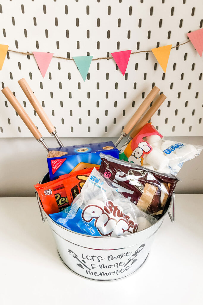 This is of an image of a s'mores metal basket with the free making smore memories SVG and s'mores supplies inside of the bucket.