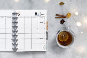 This image is of a planner open to a 2023 calendar with holidays. This is one of the options you can download at the end of this blog post. This image shows a 2023 January calendar with a Monday start. It’s open to the right side of the calendar. Next to the planner is a mug with tea, cinnamon sticks, and a string of lights.