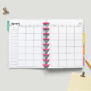 This image shows the free printable 2023 calendar you can get for free at the end of this blog post. This image shows a simple Classic Happy planner with pink discs opened up to a January 2023 monthly calendar spread.