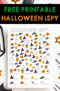At the top the image says Free Printable Halloween I Spy. Under that is an image of one of the free printable Halloween i spy worksheets you can download for free at the end of this blog post. It is surrounded by a few gold stars, part of a black web, and some fake spider legs.